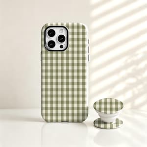 Puede incluir: Una funda para teléfono con estampado de cuadros vichy en color verde salvia y blanco, junto con un soporte circular plegable a juego. La funda presenta un recorte rectangular para una cámara triple y un borde negro.