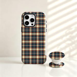 Puede incluir: Una funda para smartphone y un soporte circular a juego con un patrón de cuadros clásico en tonos azul marino, rojo oscuro y crema. La funda tiene forma rectangular con un recorte para la cámara, mientras que el soporte es redondo y plegable.