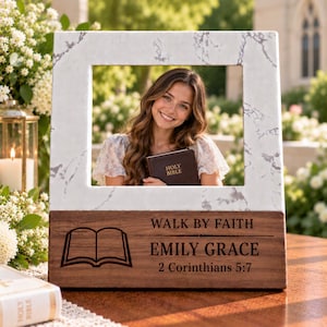 May include: A rectangular photo frame featuring a white marble-patterned top section and a dark wood base. The wood base is engraved with an open book icon, the text WALK BY FAITH, the name EMILY GRACE, and the scripture reference 2 Corinthians 5:7.