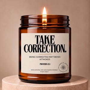 May include: A lit candle in an amber glass jar with a cream-colored label. The label features the text TAKE CORRECTION. BEING CORRECTED ISN'T BEING ATTACKED. PROVERBS 12:1, 100% NATURAL SOY WAX BLEND CANDLE, 9 OZ | 255 G, and an Arise & Asnd Candle Co. logo.