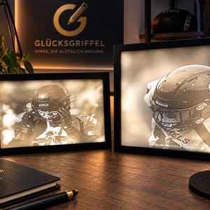 Könnte beinhalten: Zwei rechteckige Leuchtkästen mit schwarzem Rahmen zeigen sepiafarbene Bilder eines Footballspielers mit Helm. Der größere Rahmen trägt den Schriftzug BERLIN REBELS YOUTH auf dem Trikot. Die Rahmen sind von innen beleuchtet.