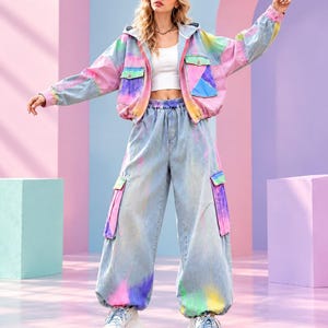 May include: A pink baseball cap, a white crop top, and a light blue denim jacket with multicoloured tie-dye panels and chest pockets. The outfit includes matching light blue denim cargo trousers with tie-dye accents and white platform trainers.