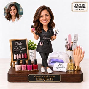 Könnte beinhalten: Eine individuelle Wackelfigur einer Nageldesignerin in schwarzer Schürze mit der Aufschrift NAILS ART BEAUTY CONFIDENCE auf einem Holzsockel mit der Gravur Creative Nail Artist Emma Brooks, umgeben von Nagellackflaschen und UV-Lampe.