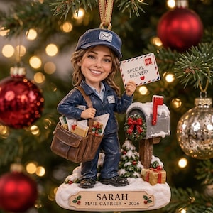 Könnte beinhalten: Eine Postboten-Figur als Weihnachtsschmuck in blauer Uniform und Mütze, die einen Umschlag mit der Aufschrift SPECIAL DELIVERY hält. Die Figur trägt eine braune Tasche voller Post und steht neben einem Briefkasten. Basis mit SARAH MAIL CARRIER 2026.