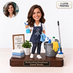 以下が含まれることがあります： Clean Brighter Happier Livesと書かれた紺色のエプロンを着用し、青いスプレーボトルを持った家政婦のカスタムボブルヘッドフィギュア。台座にはHardworking Housekeeper Emma Brooksと刻まれたプレートがあり、掃除用具が添えられています。