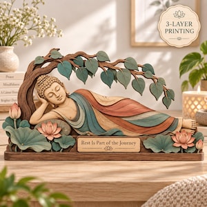 May include: A multi-layered wooden sculpture of a reclining Buddha resting under a tree with teal leaves. The base features pink lotus flowers and a plaque with the text 'Rest Is Part of the Journey'. The design uses 3-layer printing techniques.