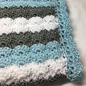 May include: A crocheted baby blanket with a scalloped edge in shades of gray, white, and light blue.