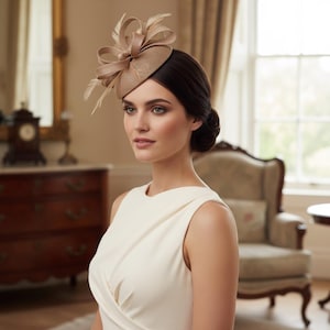 Pode incluir: Um fascinator bege com uma base circular estruturada, apresentando laços intrincados e penas delicadas. O acessório é usado de lado, exibindo um acabamento em tecido texturizado e um design sofisticado posicionado sobre a cabeça.