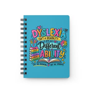 May include: A spiral-bound notebook with a bright blue cover featuring colorful text that reads: DYSLEXIA ISN'T A DISABILITY... IT'S A Different ABILITY. The design includes illustrations of a stack of books, a pencil, a brain, and an open book.