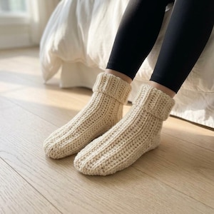 Puede incluir: Un par de calcetines tobilleros de punto grueso en color crema, con textura acanalada y diseño de puño doblado. Los calcetines están confeccionados con hilo grueso y presentan un patrón de puntada vertical desde la punta hasta el puño.