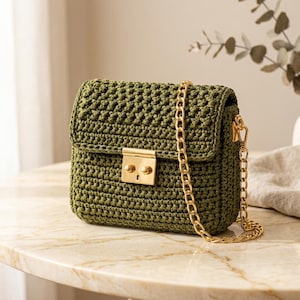 May include: A rectangular olive green crochet handbag featuring a textured stitch pattern. The bag includes a gold-toned metal rectangular push-lock closure on the front flap and a matching gold-toned metal chain shoulder strap attached to the sides.