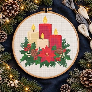 Könnte beinhalten: Ein runder Holzstickrahmen mit einem Kreuzstichmuster aus drei brennenden Kerzen in Rot und Creme, umgeben von grünen Tannennadeln, roten Beeren und einem zentralen roten Weihnachtsstern mit braunen Tannenzapfen.