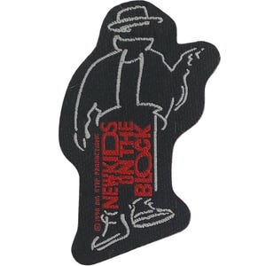 Könnte beinhalten: Ein schwarzer gestickter Aufnäher mit dem weißen Umriss einer Person mit Hut und Jacke. Der Text NEW KIDS ON THE BLOCK ist in Rot gestickt, darunter befindet sich der Copyright-Text 1990 BIG STEP PRODUCTIONS und ein kleines weißes Schuhsymbol.