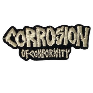 Op de afbeelding: Een zwarte geborduurde patch met de tekst CORROSION OF CONFORMITY in een gestileerd, grillig wit lettertype. De letters zijn geborduurd met een dikke, getextureerde draad, wat zorgt voor een reliëf op de zwarte stoffen achtergrond.