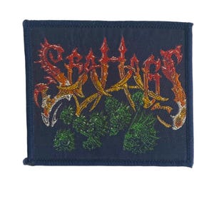 Op de afbeelding: Een rechthoekige geborduurde patch op een donkerblauwe stoffen ondergrond. De patch bevat de tekst "SEAHAGS" in een gestileerd, grillig rood en oranje lettertype. Onder de tekst bevindt zich een geborduurde afbeelding van groene, getextureerde plantachtige clusters.