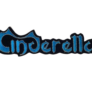 Puede incluir: Un parche de tela negra con la palabra Cinderella bordada en hilo azul brillante con un contorno plateado metálico. Las letras están estilizadas en una fuente cursiva y el parche está cortado siguiendo la forma del texto.