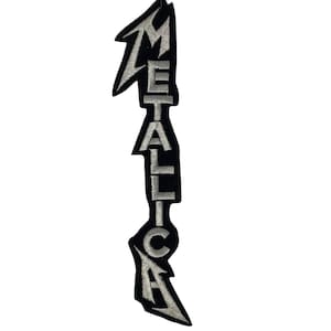 Op de afbeelding: Een verticale geborduurde patch met het woord Metallica in zilverdraad op een zwarte achtergrond. De letters zijn gerangschikt in een gestileerd, grillig lettertype waarbij de M en A uitlopen in scherpe punten voor een smal ontwerp.