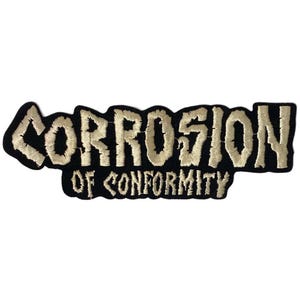 May include: A rectangular embroidered patch featuring the text CORROSION OF CONFORMITY in a jagged, distressed beige font against a solid black background. The lettering is arranged in two lines with a distinct, rough-edged style.