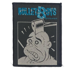 Op de afbeelding: Een rechthoekige zwarte geborduurde patch met de blauwe tekst BULLET BOYS bovenaan. Onder de tekst staat een grijze afbeelding van een stripfiguur met een wc-rol op het hoofd. De tekst 1989 BULLET BOYS is in kleine blauwe letters gedrukt.