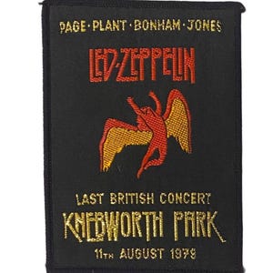Op de afbeelding: Een rechthoekige zwarte geborduurde patch met de tekst PAGE PLANT BONHAM JONES bovenaan, het Led Zeppelin-logo in rood, een centrale gevleugelde figuur in rood en goud, en de tekst LAST BRITISH CONCERT KNEBWORTH PARK 11TH AUGUST 1979.