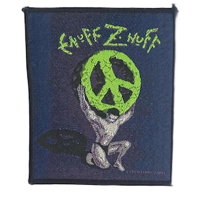 May include: A rectangular embroidered patch with a dark blue background. It features a figure kneeling and holding a large, textured lime green peace sign above their head. The text "ENUFF Z'NUFF" is embroidered in lime green above the figure.