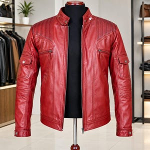 May include: A vibrant red leather jacket featuring a stand-up collar with snap buttons, a full-length front zip, and quilted shoulder detailing. The jacket includes two zipped chest pockets, two lower flap pockets with snap closures, and buttoned cuffs.