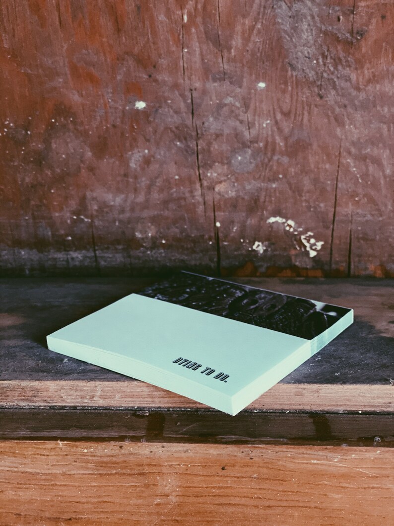 May include: A light blue notepad with the text "DIY TO DO." printed on the front. The notepad is sitting on a wooden surface.
