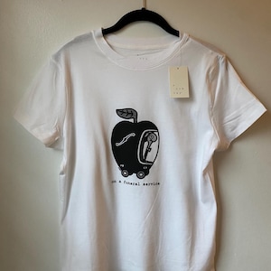 Könnte beinhalten: Weißes T-Shirt mit einer schwarz-weißen Illustration eines Apfels mit einer Person darin, auf Rädern, und dem Text "on a funeral service".