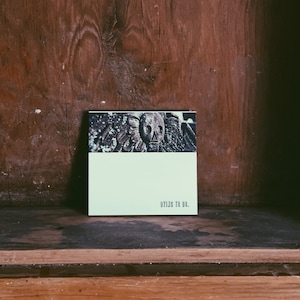 May include: A small, white card with a skull image and the text "Dying to Do." The card is sitting on a wooden shelf.