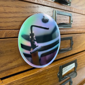 May include: A round iridescent sticker with a photo of a silver faucet with a black background.