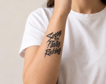 May include: A temporary tattoo applied to the forearm featuring the black text Sorry for Party Rocking in a stylized, angular, and bold font. The design is positioned vertically on the skin, showcasing sharp, jagged lettering.