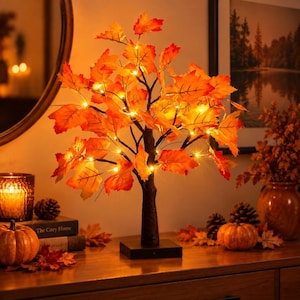 Könnte beinhalten: Ein dekorativer Tischbaum mit künstlichen orangefarbenen und roten Ahornblättern, beleuchtet durch kleine warmweiße LED-Lichter. Der Baum hat einen dunkelbraunen, strukturierten Stamm und einen quadratischen Sockel für herbstliche Akzente.
