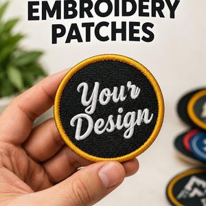 Peut inclure: Un écusson brodé noir de forme circulaire avec une bordure dorée cousue et le texte blanc Your Design écrit en police cursive. L'écusson est présenté devant un arrière-plan affichant le texte Custom Embroidery Patches, Best Quality et Bulk Discounts.