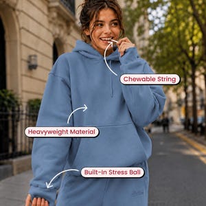 May include: A blue hooded sweatshirt made of heavyweight material featuring a chewable string near the neckline and a built-in stress ball integrated into the sleeve cuff. The garment includes a front kangaroo pocket and matching blue sweatpants.