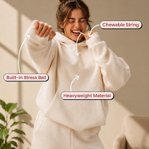 Può includere: Una felpa con cappuccio color crema in materiale pesante, dotata di una pallina antistress integrata nella manica e di un cordino masticabile vicino allo scollo. Il capo presenta una tasca a marsupio frontale e maniche lunghe con polsini.