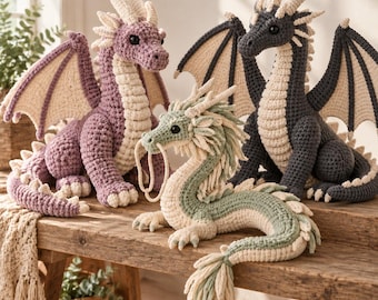 May include: Three crocheted dragon plush toys in different colors. One is dusty purple, one is dark charcoal gray, and one is sage green. Each dragon features cream-colored accents on the wings, underbelly, horns, and tail spikes with black eyes.