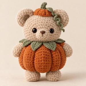 May include: A beige crochet bear plush toy wearing a pumpkin costume. The bear has black eyes and a brown nose. The pumpkin suit features a ribbed orange body, a green leaf collar, and a small orange pumpkin hat with a green vine.