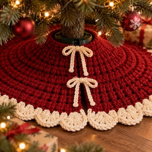 Puede incluir: Una falda de &aacute;rbol de Navidad tejida a ganchillo en color rojo oscuro con un borde festoneado grueso de color crema y dos lazos de ganchillo a juego en color crema para cerrar la abertura alrededor del tronco.