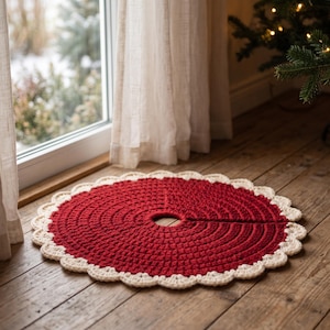 Puede incluir: Una falda de &aacute;rbol de Navidad circular tejida a ganchillo, con un centro rojo intenso y un borde festoneado de color crema. El accesorio textil tiene una abertura central y una ranura recta que se extiende hasta el borde.