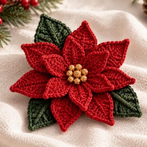 May include: A crocheted poinsettia ornament featuring layered red petals and dark green leaves. The centre of the flower is adorned with a cluster of small, round, metallic gold beads. The texture of the yarn is visible throughout the petals and leaves.