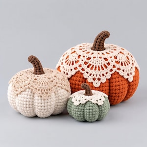 May include: Three crocheted pumpkins in varying sizes and colors. The largest is orange, the medium is cream, and the smallest is sage green. Each pumpkin features a brown crocheted stem and a decorative cream-colored lace doily topper.