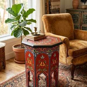 Può includere: Un tavolino ottagonale caratterizzato da una base rossa con intricati motivi floreali e geometrici dipinti a mano in blu, verde, giallo e bianco. Il tavolo presenta una superficie superiore piatta e aperture ad arco alla base di ogni lato.
