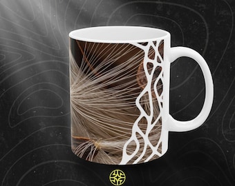 Puede incluir: Una taza de cerámica blanca con una impresión fotográfica de alta resolución de semillas de algodoncillo marrones con delicados filamentos blancos y sedosos. Una superposición gráfica blanca tipo red cubre parcialmente la imagen. Texto ASSEMBLE WONDER.