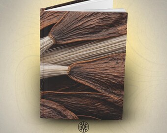 Puede incluir: Un libro de tapa dura con una portada que muestra un primer plano de vainas de semillas de color marrón oscuro con textura y fibras de color beige claro. El libro está ligeramente abierto, revelando páginas blancas. El texto ASSEMBLE WONDER está impreso en la parte inferior.