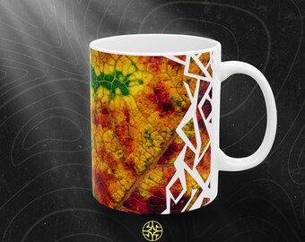 Puede incluir: Una taza de cerámica blanca con un patrón de hojas de otoño en tonos amarillo, naranja, rojo y verde, superpuesto con un diseño geométrico blanco en el lado derecho. El texto ASSEMBLE WONDER aparece debajo de la taza.