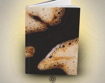 Puede incluir: Un libro de tapa dura con una impresión fotográfica de alta resolución de café negro con burbujas de espuma de color marrón claro en la portada. El libro está ligeramente abierto en la parte superior, revelando páginas blancas. ASSEMBLE WONDER está impreso.