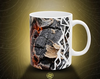 Puede incluir: Una taza de cerámica blanca con una impresión fotográfica de brasas naranjas brillantes y leños de madera negra carbonizada, contrastada por un patrón geométrico de líneas blancas, con el texto ASSEMBLE WONDER impreso debajo de la taza.
