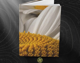 Puede incluir: Un libro de tapa dura que presenta una fotografía macro de una margarita blanca con un centro amarillo en la portada. La parte inferior de la portada muestra un logotipo circular amarillo sobre el texto ASSEMBLE WONDER en letras mayúsculas.