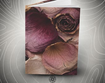 Puede incluir: Un libro de tapa dura con una impresión fotográfica de pétalos de rosa secos en tonos púrpura apagado y rosa polvoriento en la portada. El libro está ligeramente abierto, mostrando páginas blancas. Debajo, el texto ASSEMBLE WONDER con un logo.