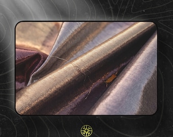 Puede incluir: Una pieza de tela iridiscente con tonos profundos de bronce, cobre y morado oscuro. El material muestra un brillo metálico con texturas de tejido horizontal visibles y pliegues suaves que crean luces y sombras sobre la superficie.